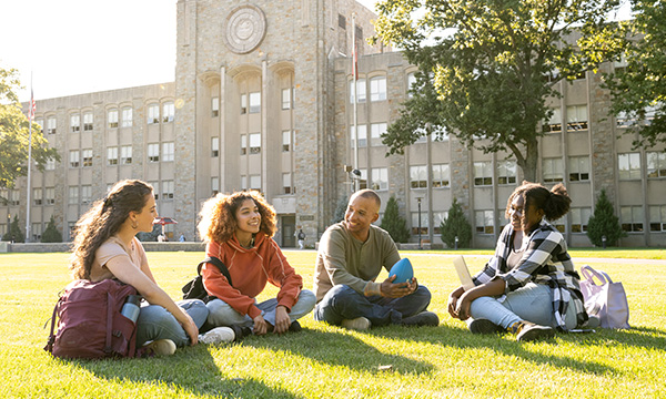 A couple of kids sitting in the grass around a campus building