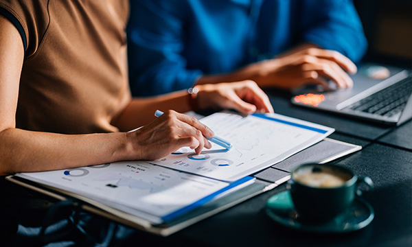 An image focusing on two people touching on a document with charts